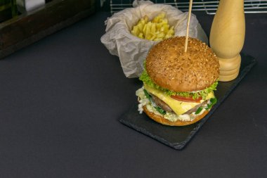 Grafit standında yakın plan hamburger, yanında patates kızartması, domates ve biber, arkasında ızgara rafı var. Açık alanlı en üstteki görünüm