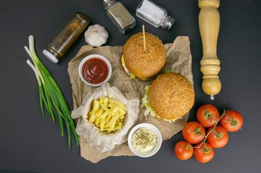 Yakın planda iki hamburger, kızartma, domates, sos, domates ve biber var. Arka planda ızgara rafı.