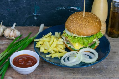 Mavi tabakta yakın plan hamburger, yanında doğranmış soğan, patates kızartması ve ketçap..