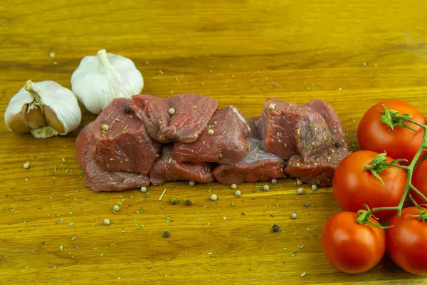 在西红柿和大蒜旁边的木板上 放着切碎的多汁牛肉片 — 图库照片