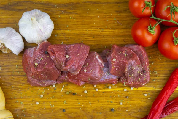 在西红柿和大蒜旁边的木板上 放着切碎的多汁牛肉片 — 图库照片