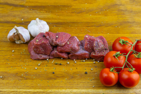 Sliced juicy slices of veal stand on a wooden board, next to tomatoes and garlic.