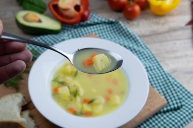 Patatesli, havuçlu, yeşillikli beyaz süt çorbası tahta bir tabakta duruyor..