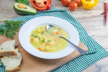 Patatesli, havuçlu, yeşillikli beyaz süt çorbası tahta bir tabakta duruyor..