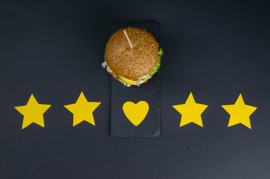 Siyah arka planda 5 yıldız ve kalp değeriyle izole edilmiş bir burger. Sarı yıldızlar. Üst Görünüm