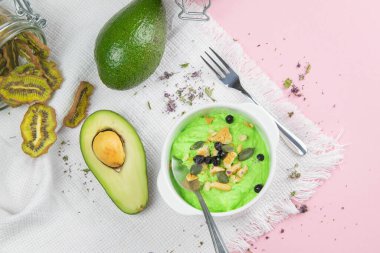 Avokado ve kiviyle kaymak. Sağlıklı beslenme konsepti. Pembe arka planda kaselerde çeşitli ürünler.