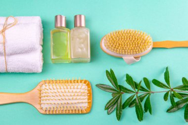 Üç havlu, vücut bakım yağı, yeşil bir dal, filiz ve yeşil arka planda bir fırça standı. Spa tedavisi kavramı, sağlıklı bir vücut..