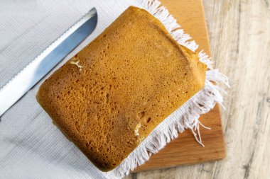 Taze ev yapımı ekmek, ekmek kesmek için kullanılan bıçağın yanında, tahta bir tahtanın üzerinde beyaz bir havlu üzerinde duruyor. Üst Görünüm.