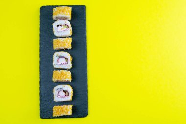 Suşi dolu granit pano, suşi çubukları, kırmızı marinaginger ve sarı arka planda soya sosu. Açık alanlı en üstteki görünüm