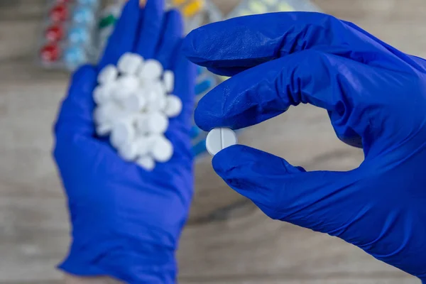 Many small white pills in the hands of a doctor wearing medical blue disposable gloves. Hands take one pills.