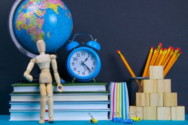 Küre ve saat bir kitap yığınının üzerinde duruyor, bir bardak kalemin yanında ve piramit ahşap küplerle ve ahşap bir adam figürüyle katlanmış..