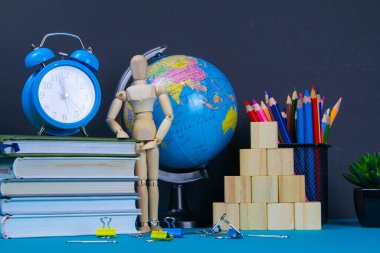 Küre ve saat bir kitap yığınının üzerinde duruyor, bir bardak kalemin yanında ve piramit ahşap küplerle ve ahşap bir adam figürüyle katlanmış..