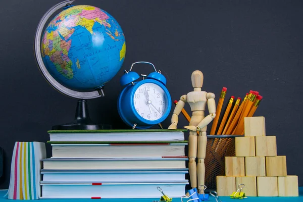 Küre ve saat bir kitap yığınının üzerinde duruyor, bir bardak kalemin yanında ve piramit ahşap küplerle ve ahşap bir adam figürüyle katlanmış..