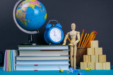 Küre ve saat bir kitap yığınının üzerinde duruyor, bir bardak kalemin yanında ve piramit ahşap küplerle ve ahşap bir adam figürüyle katlanmış..