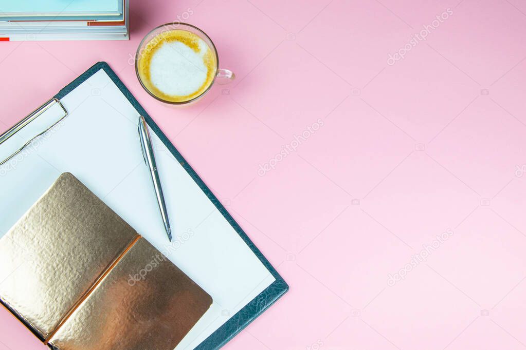 The pen and gold notebook stand on a tablet with a white sheet next to a glass of coffee.