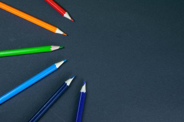 Siyah arkaplan üzerinde izole edilmiş bir dalgada dizilmiş renkli kalemler.