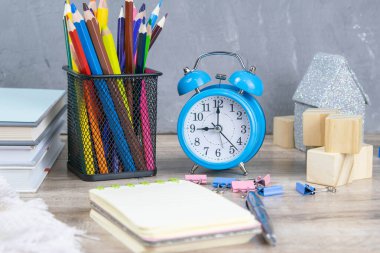 Bir yığın kitap, bir saat, piramit şeklinde ahşap küpler, yanında şeffaf cam bardakta limonlu çay ve çok renkli kalemler..