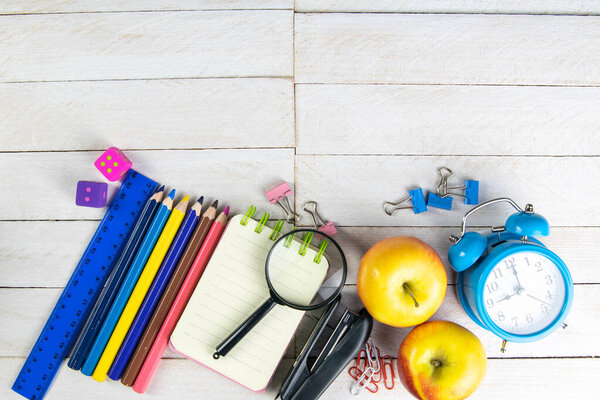 Various office stationery, notepad, clock, pencils, ooh, glasses, pen and two fresh apples on a white wooden table. Top view with copy space. Concept of office, education, workplace, school.