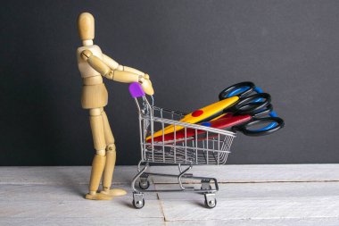 Alışveriş konsepti. Kırtasiye makası dolu sepeti olan tahta bir adam figürü..