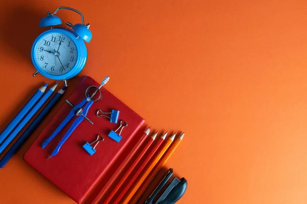 Rood Notitieboekje Met Potloden Kompas Nietmachine Klok Een Oranje Achtergrond — Stockfoto