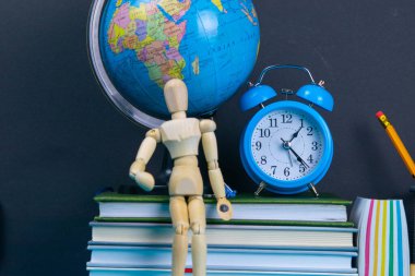 Küre ve saat bir kitap yığınının üzerinde duruyor, bir bardak kalemin yanında ve piramit ahşap küplerle ve ahşap bir adam figürüyle katlanmış..