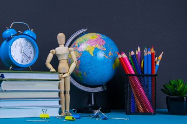 Küre ve saat bir kitap yığınının üzerinde duruyor, bir bardak kalemin yanında ve piramit ahşap küplerle ve ahşap bir adam figürüyle katlanmış..