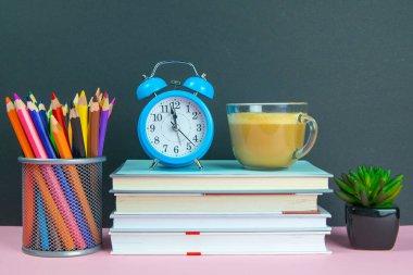 Yanında süt olan bir kahvenin bulunduğu bir yığın kitap yeşil bir çiçek ve kalemlerle dolu bir bardak..