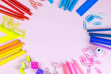 Çok renkli kalemler, cetvel, kalem, kalem, makas ve kırtasiye tezgahları pembe arka planda..