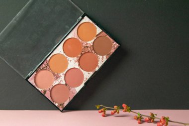 Makyaj için çok renkli gölgeler pembe bir masanın üzerinde duruyor ve siyah bir duvara dayanıyor..