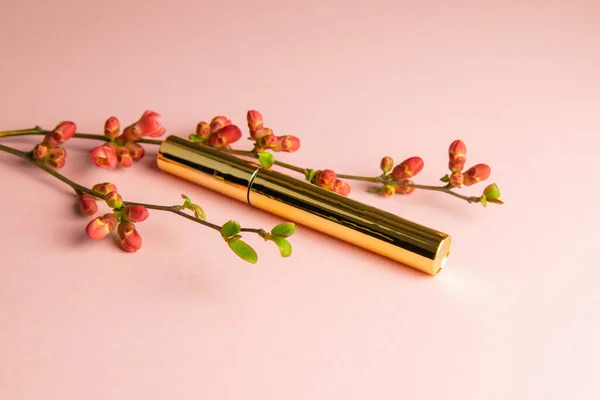The brush and eyelash paint is placed with a flowering branch with pink flowers on a pink background. Top views