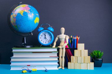 Küre ve saat bir kitap yığınının üzerinde duruyor, bir bardak kalemin yanında ve piramit ahşap küplerle ve ahşap bir adam figürüyle katlanmış..