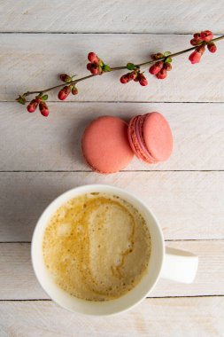 Sütlü kahve, pembe kekler ve beyaz ahşap bir masada pembe çiçek standı..