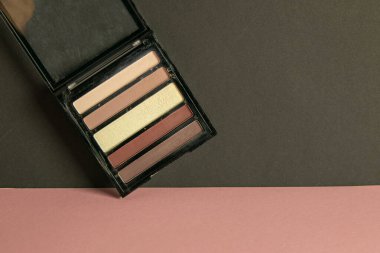 Makyaj için çok renkli gölgeler pembe bir masanın üzerinde duruyor ve siyah bir duvara dayanıyor..