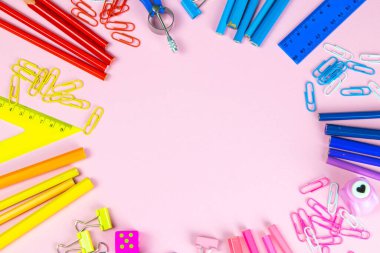 Çok renkli kalemler, cetvel, kalem, kalem, makas ve kırtasiye tezgahları pembe arka planda..