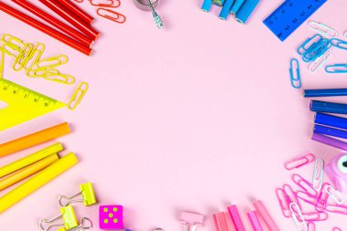 Çok renkli kalemler, cetvel, kalem, kalem, makas ve kırtasiye tezgahları pembe arka planda..