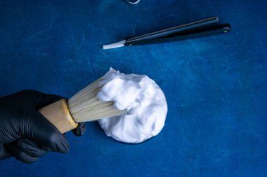 Sakala köpük sürmek için el fırçası, köpük ve mavi arka planda tehlikeli jilet. Kuaför konsepti.