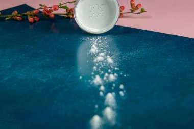 Makyaj için pudra ve gül çiçekli çiçek dalı pembe-mavi arka planda duruyor..