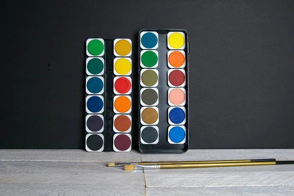 Πολύχρωμα Χρώματα Στέκονται Ένα Ξύλινο Τραπέζι Στηριγμένο Έναν Μαύρο Τοίχο — Φωτογραφία Αρχείου