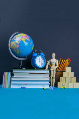 Küre ve saat bir kitap yığınının üzerinde duruyor, bir bardak kalemin yanında ve piramit ahşap küplerle ve ahşap bir adam figürüyle katlanmış..