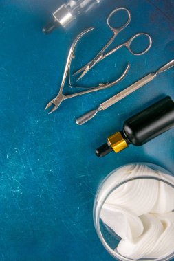Mavi arka planda manikür ve pedikür için bir takım kozmetik aletler. Manikür makası, tırnak eti, testere, değirmenci ve el yağı..