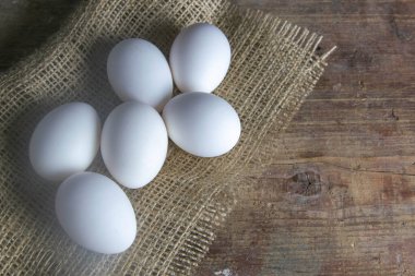 Beyaz yumurtalar ahşap bir masada bir çuval bezi üzerinde duruyor. Açık alanlı en üstteki görünüm