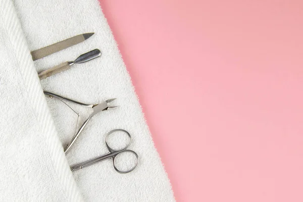 A set of cosmetic tools for manicure and pedicure. Manicure scissors, cuticles, saws on white towel stand on a pink background. Top views with clear space