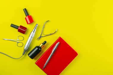 Manikür ve pedikür için kozmetik aletler. Manikür makası, tırnak makasları, testereler, değirmenci ve kırmızı defter arka planda duruyor. Açık alanlı en üstteki görünüm