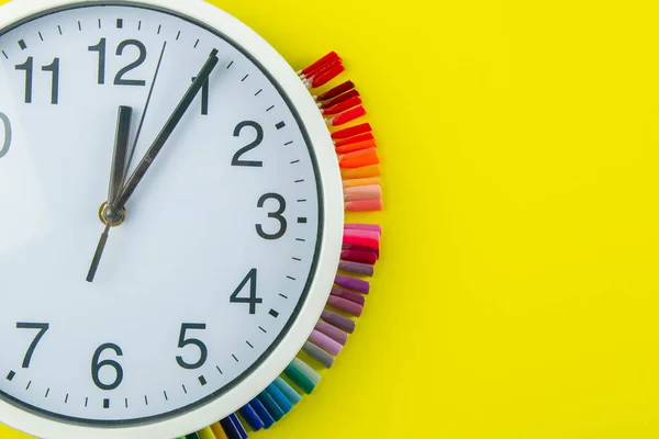 A set of cosmetic tools for manicure and pedicure on a blue background. The watch and palette of colors for manicureons on tips stands under the clock all standing on a yellow background