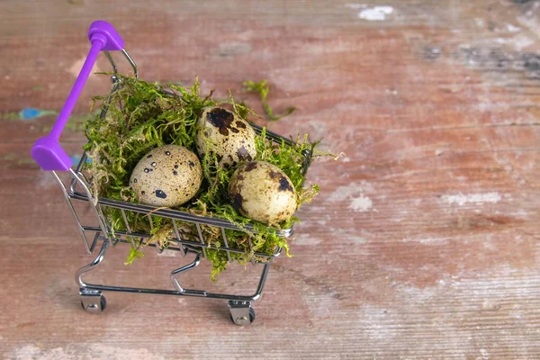 Quail eggs stand in a basket of supermarket filled with moss stand on a wooden table. Top views with clear space.
