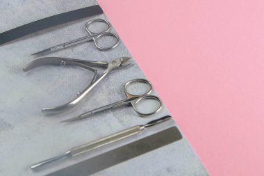 Manikür ve pedikür için kozmetik aletler. Manikür makası, tırnak eti, testere, değirmenci beton pembe arka planda duruyor. Açık alanlı en üstteki görünüm.