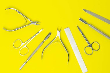 Manikür ve pedikür için kozmetik aletler. Manikür makası, makas, tırnak makası sarı arka planda duruyor. Açık alanlı en üstteki görünüm.