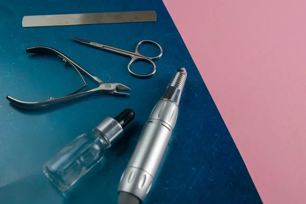 A set of cosmetic tools for manicure and pedicure. Manicure scissors, cuticles, saws, miller stand on a blue and pink background. Top views with clear space.
