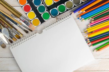Sanatçı aksesuar koleksiyonu. Tablo, boya tüpü, sanat fırçaları palet bıçağı ve ahşap masanın üzerinde duran beyaz defter. Sanatçı atölyesi arka planı.
