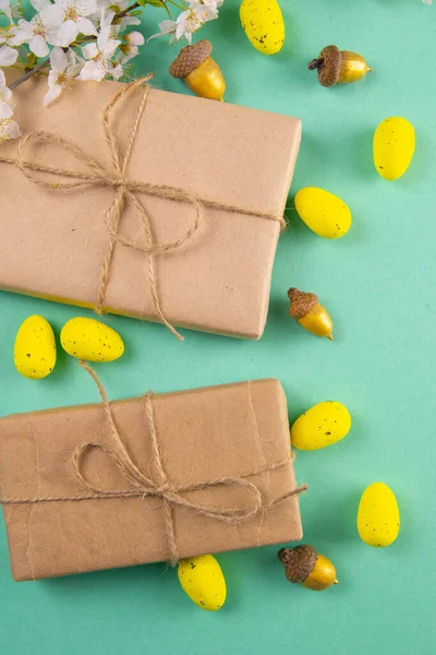 Two easter gifts, yellow eggs and white spring flowers on a mint background close-up. Easter background.